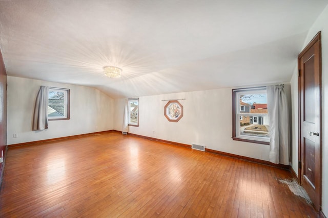 interior space featuring lofted ceiling, visible vents, baseboards, and wood-type flooring