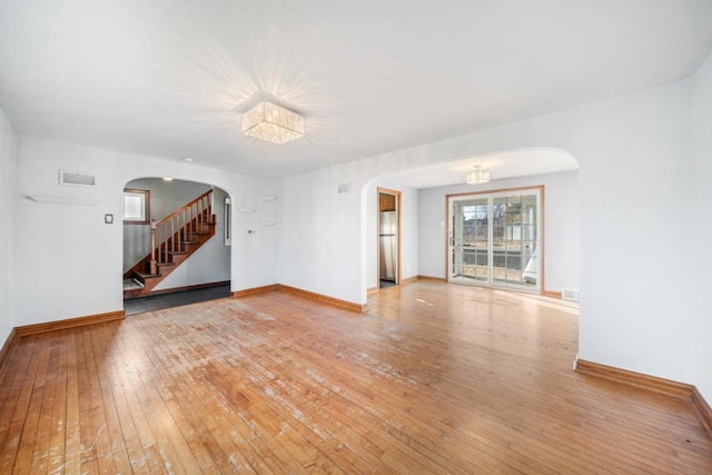 unfurnished living room featuring visible vents, baseboards, stairs, light wood-style floors, and arched walkways