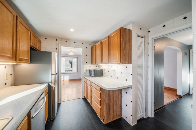 kitchen with brown cabinets, dark wood finished floors, stainless steel appliances, arched walkways, and light countertops