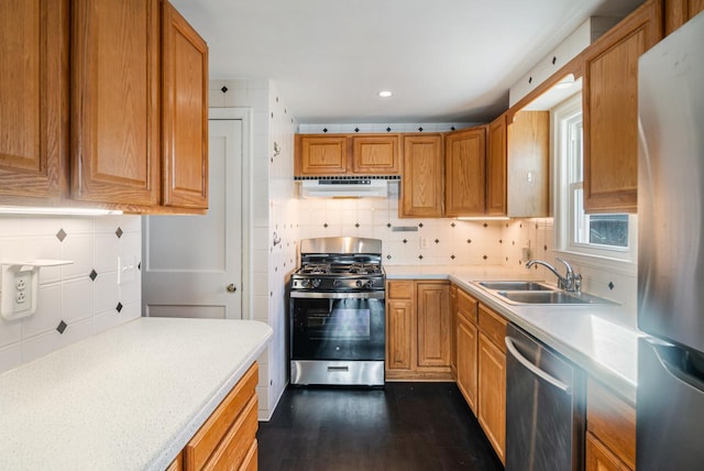 kitchen featuring backsplash, under cabinet range hood, light countertops, appliances with stainless steel finishes, and a sink