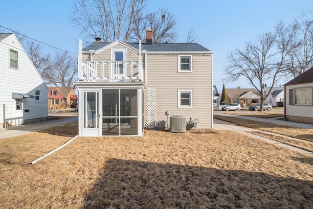 rear view of property featuring central AC unit, a chimney, a balcony, and a sunroom