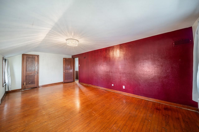 empty room with visible vents, lofted ceiling, baseboards, and wood-type flooring