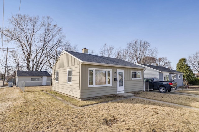 view of front of home with board and batten siding, a front lawn, fence, roof with shingles, and a chimney