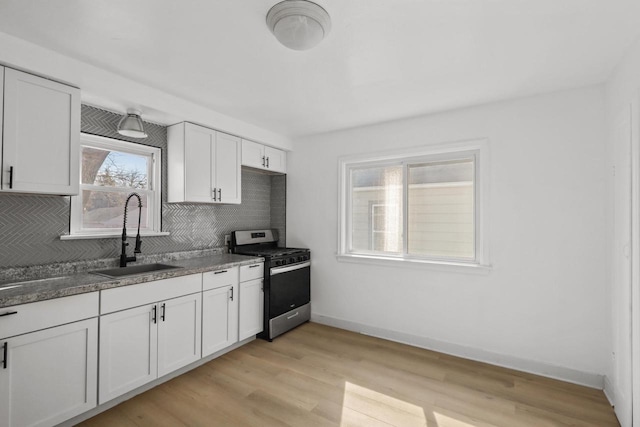 kitchen featuring stainless steel gas range oven, white cabinetry, backsplash, and a sink