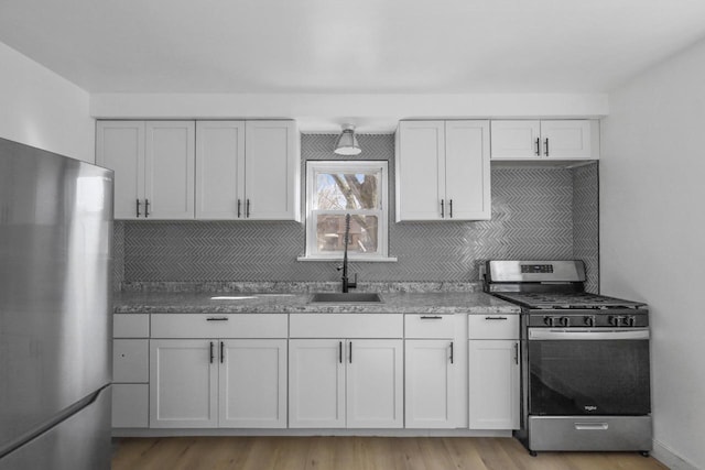 kitchen featuring light wood-style flooring, tasteful backsplash, appliances with stainless steel finishes, and a sink