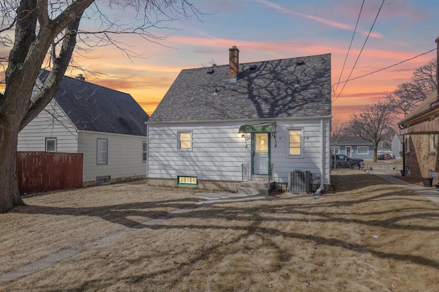 rear view of house with entry steps, fence, roof with shingles, central AC unit, and a chimney