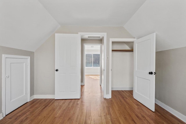 unfurnished bedroom featuring lofted ceiling, wood finished floors, baseboards, and a closet