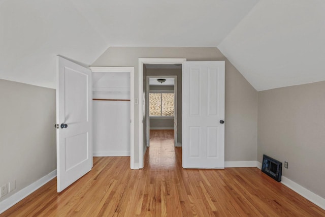 unfurnished bedroom featuring baseboards, lofted ceiling, and light wood-style floors