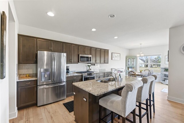 kitchen with dark brown cabinets, decorative backsplash, light wood-style floors, and appliances with stainless steel finishes