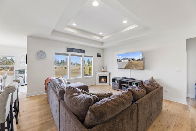 living room featuring a tray ceiling, light wood-style flooring, and a lit fireplace