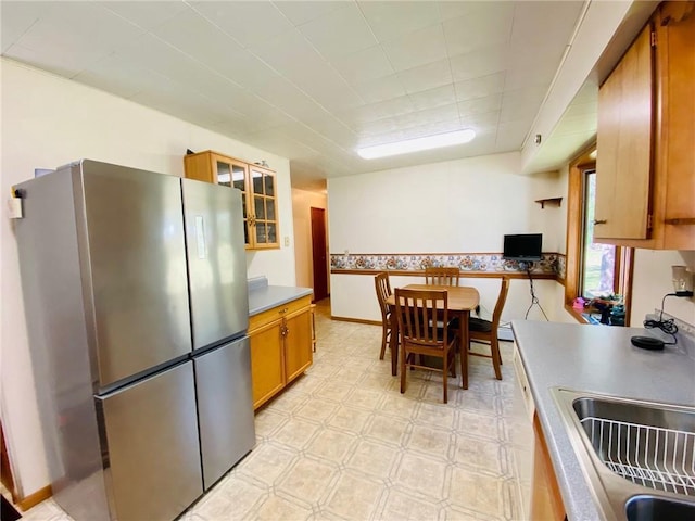 kitchen featuring a sink, freestanding refrigerator, brown cabinetry, glass insert cabinets, and light floors