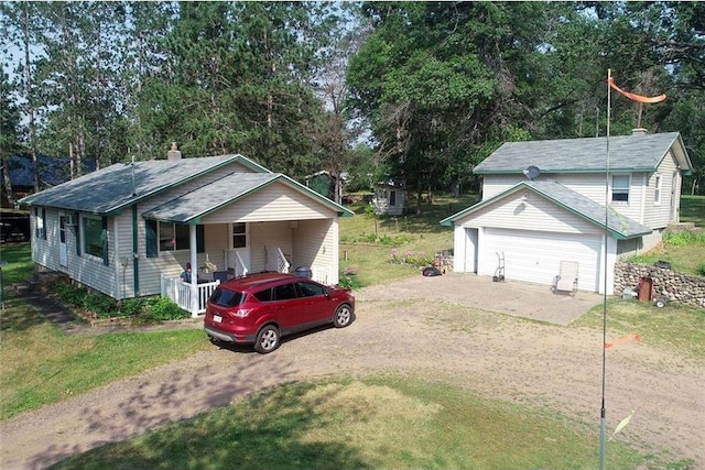 view of front facade featuring an outbuilding, dirt driveway, covered porch, a front yard, and a garage