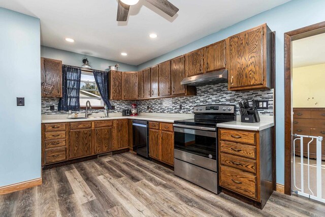 kitchen featuring under cabinet range hood, dishwashing machine, stainless steel range with electric cooktop, dark wood-style floors, and a sink