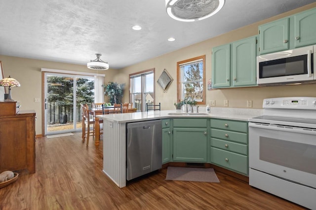 kitchen featuring a sink, light countertops, a peninsula, white appliances, and dark wood-style flooring