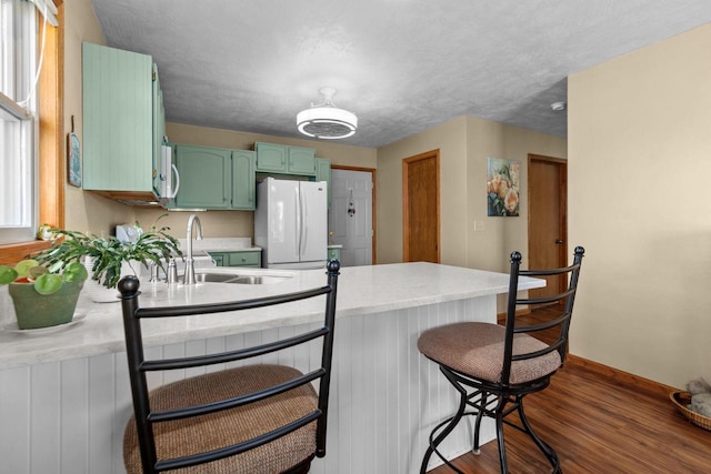 kitchen featuring white appliances, green cabinetry, a peninsula, a sink, and dark wood-type flooring