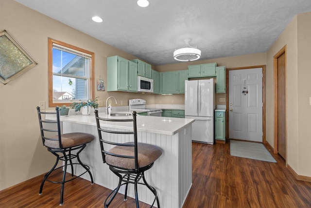 kitchen featuring white appliances, a peninsula, dark wood-style flooring, light countertops, and green cabinets