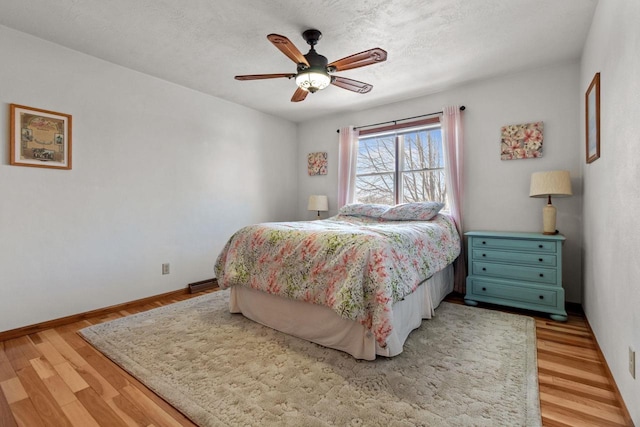 bedroom with light wood-style flooring, a textured ceiling, baseboards, and ceiling fan