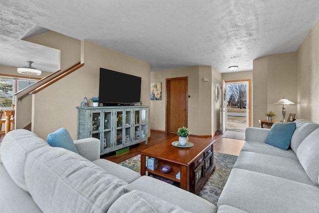 living room featuring a textured ceiling, stairs, baseboards, and wood finished floors