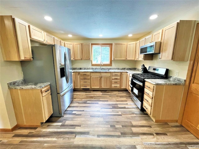 kitchen with light brown cabinets, light wood finished floors, a sink, stainless steel appliances, and a textured ceiling