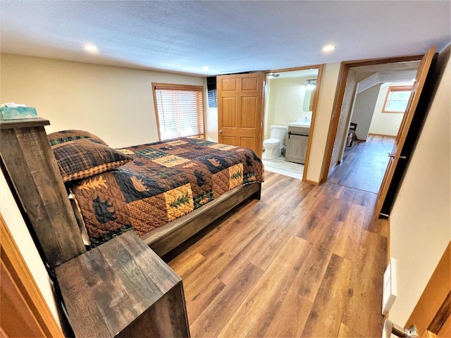 bedroom with connected bathroom, baseboards, recessed lighting, light wood-style flooring, and a textured ceiling