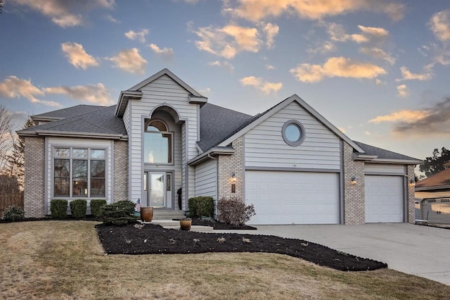 traditional-style house featuring driveway, an attached garage, a shingled roof, a lawn, and brick siding