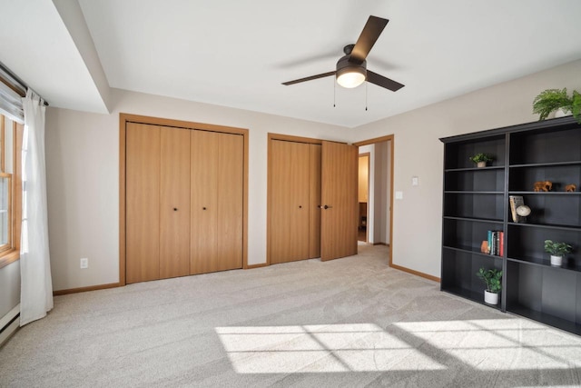 unfurnished bedroom with baseboards, multiple closets, light colored carpet, and ceiling fan