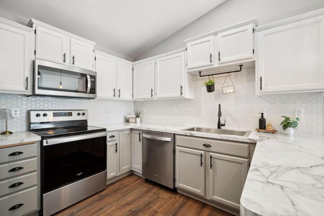 kitchen with dark wood finished floors, lofted ceiling, light stone counters, stainless steel appliances, and a sink