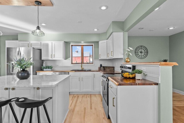 kitchen featuring a sink, appliances with stainless steel finishes, white cabinets, light wood finished floors, and wooden counters