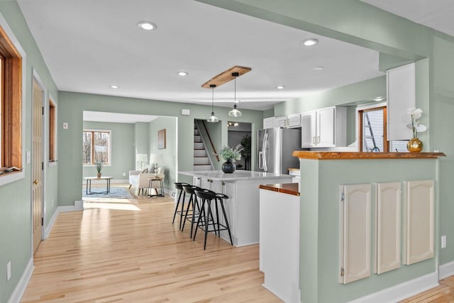 kitchen featuring a kitchen breakfast bar, white cabinets, light wood-type flooring, and freestanding refrigerator