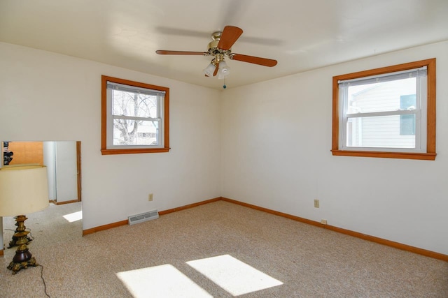 carpeted empty room with a ceiling fan, a healthy amount of sunlight, visible vents, and baseboards