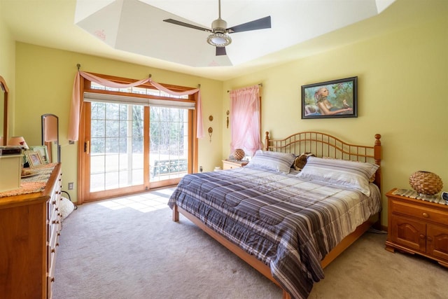 bedroom with ceiling fan, a tray ceiling, access to outside, and light carpet