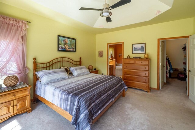 bedroom with baseboards, a tray ceiling, ensuite bath, ceiling fan, and light carpet