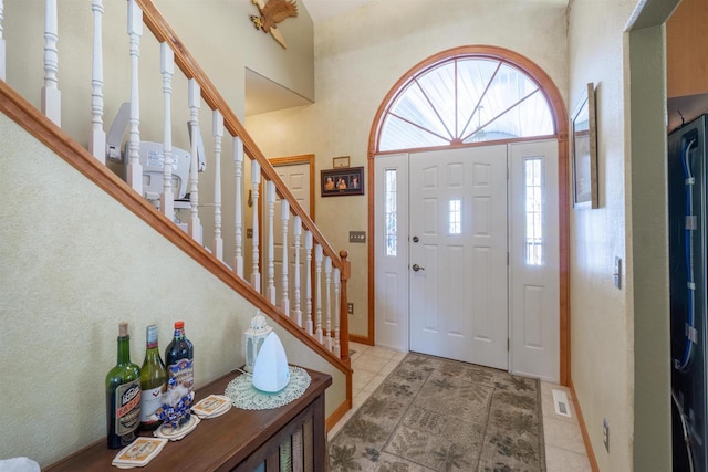 entrance foyer featuring visible vents, baseboards, stairs, light tile patterned floors, and a towering ceiling