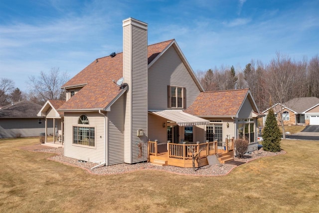 back of property with a yard, a wooden deck, a chimney, and a shingled roof