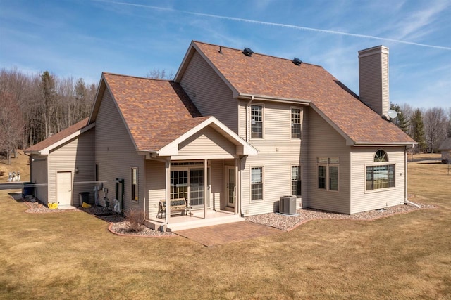 rear view of house featuring a patio, a yard, a shingled roof, a chimney, and central air condition unit