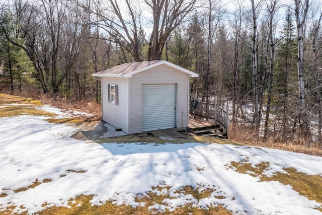 snow covered garage with a garage, a wooded view, and a shed