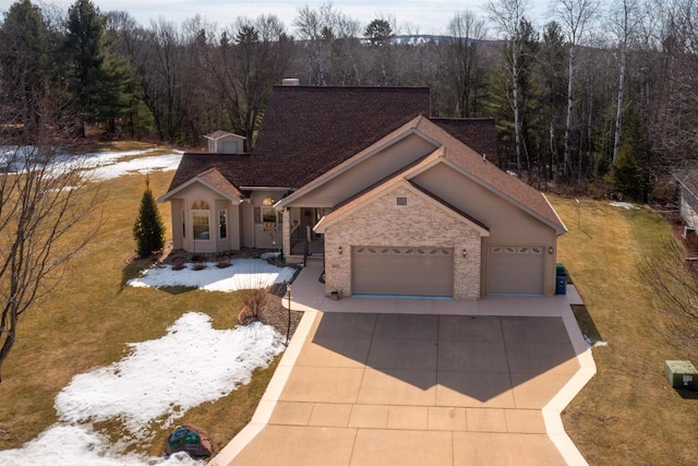 view of front of house featuring driveway, a yard, a wooded view, a garage, and brick siding