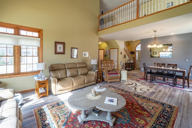 living area featuring baseboards, a notable chandelier, wood finished floors, and a towering ceiling