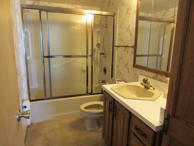 bathroom with bath / shower combo with glass door, toilet, vanity, and wallpapered walls