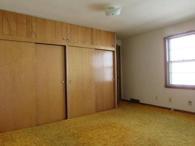 unfurnished bedroom featuring a closet, light carpet, baseboards, and visible vents