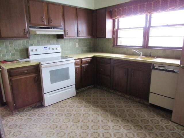 kitchen featuring under cabinet range hood, light countertops, decorative backsplash, white appliances, and a sink