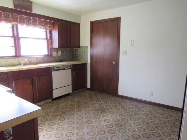 kitchen featuring tasteful backsplash, baseboards, dishwasher, light countertops, and a sink