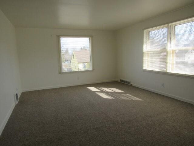 empty room with carpet flooring, a healthy amount of sunlight, visible vents, and baseboards