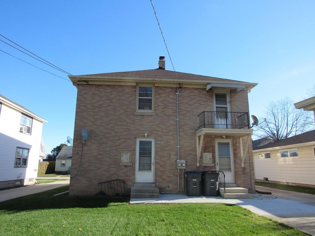 back of property featuring brick siding, entry steps, a lawn, a chimney, and a balcony