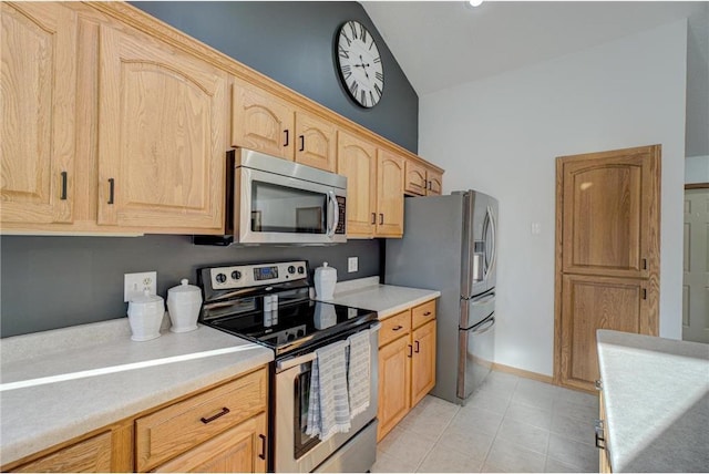 kitchen featuring light brown cabinetry, light countertops, lofted ceiling, light tile patterned floors, and appliances with stainless steel finishes