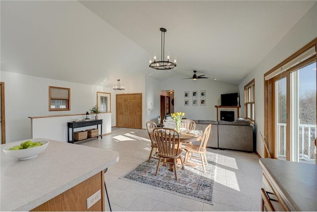 dining space with lofted ceiling, ceiling fan with notable chandelier, a fireplace, light tile patterned floors, and baseboards