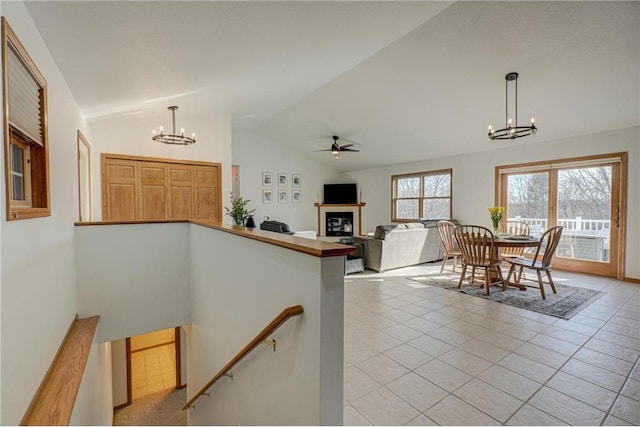 interior space with tile patterned flooring, a glass covered fireplace, ceiling fan with notable chandelier, and vaulted ceiling