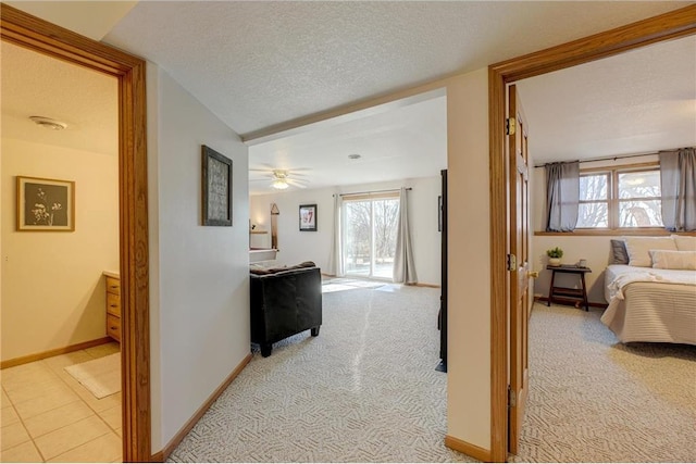 hall featuring light carpet, a textured ceiling, and baseboards