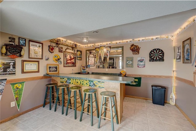 bar with tile patterned floors, baseboards, and wet bar