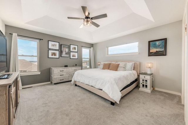 bedroom with a tray ceiling, light carpet, baseboards, and a ceiling fan